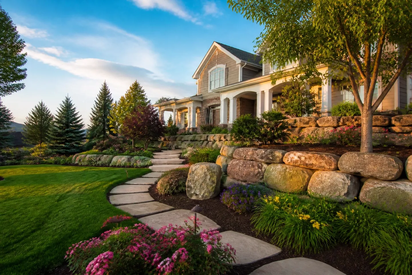 Landscaped yard with lawn, mulch beds, a boulder wall and a stone pathway